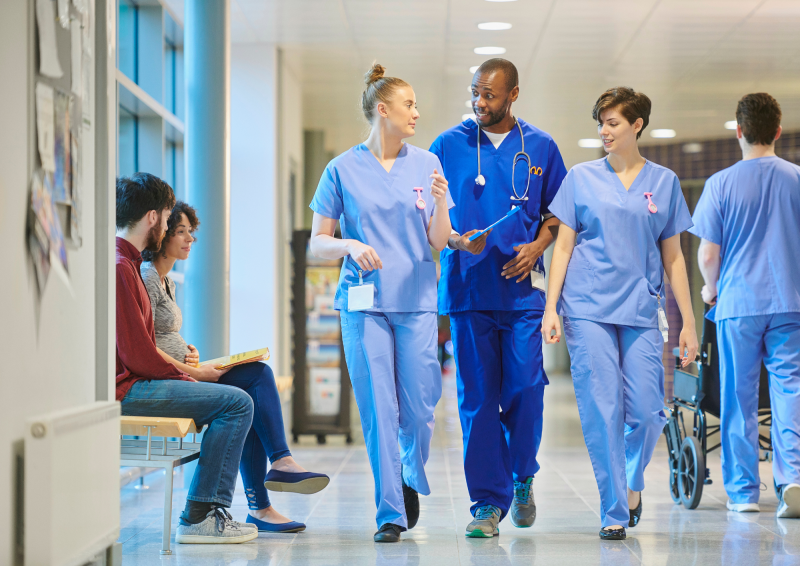 NHS doctors wearing scrubs walking through busy hospital corridor