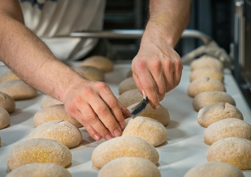 Baker scoring unbaked bread rolls